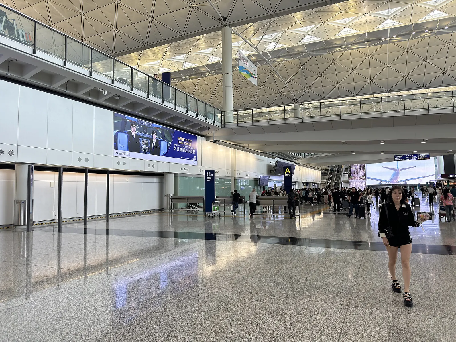 Široká příletová hala s vysokou vzorovanou střechou na mezinárodním letišti Hongkong