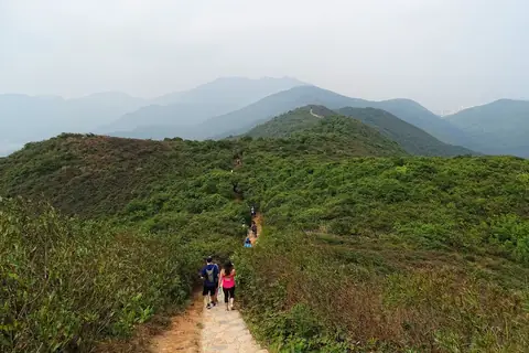 Turisté na zeleném hřebeni Dragon’s Back pod zamlženou oblohou