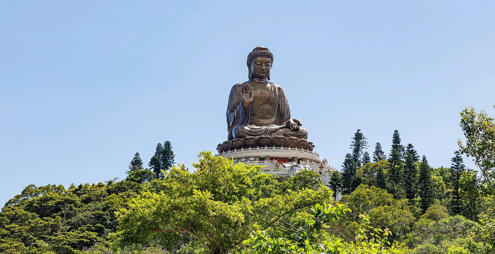 Tian Tan-Buddha over grønne træer mod en blå himmel