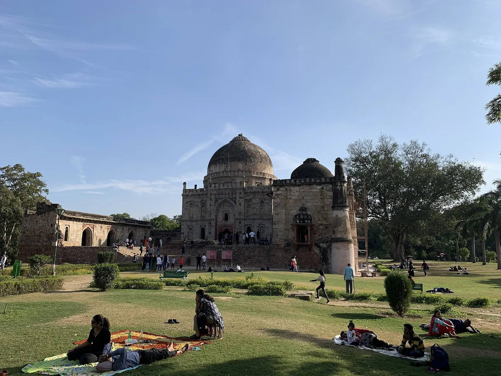Das Grabmal Bara Gumbad im Lodhi-Garten in Delhi hinter Rasenflächen, auf denen Besucher im Gras ruhen