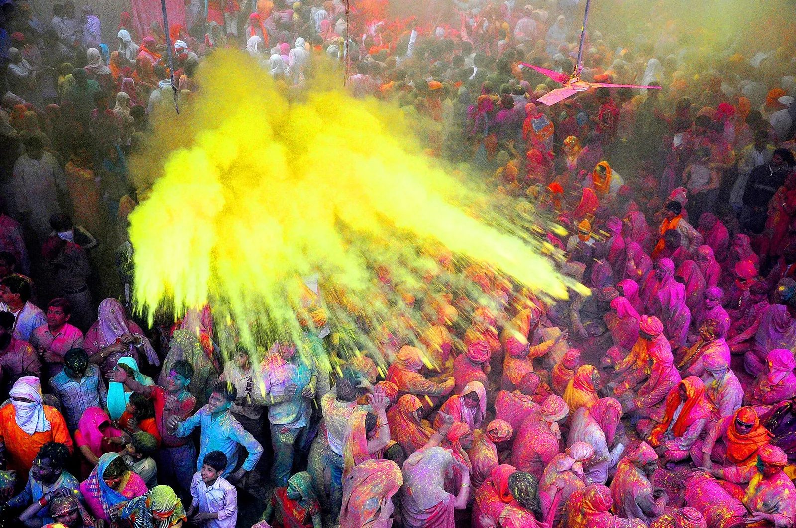 Una nube de polvo amarillo lanzada sobre una multitud compacta cubierta de colores en Holi