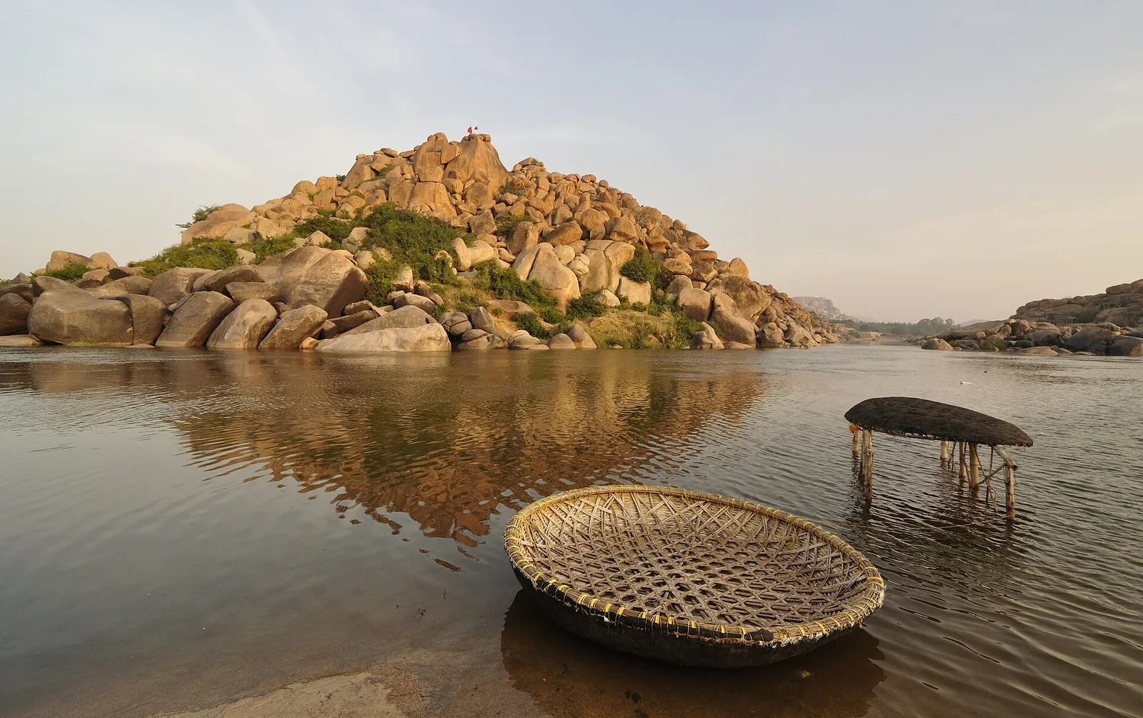 Două bărci rotunde pe râul Tungabhadra, sub un deal de bolovani, lângă Hampi