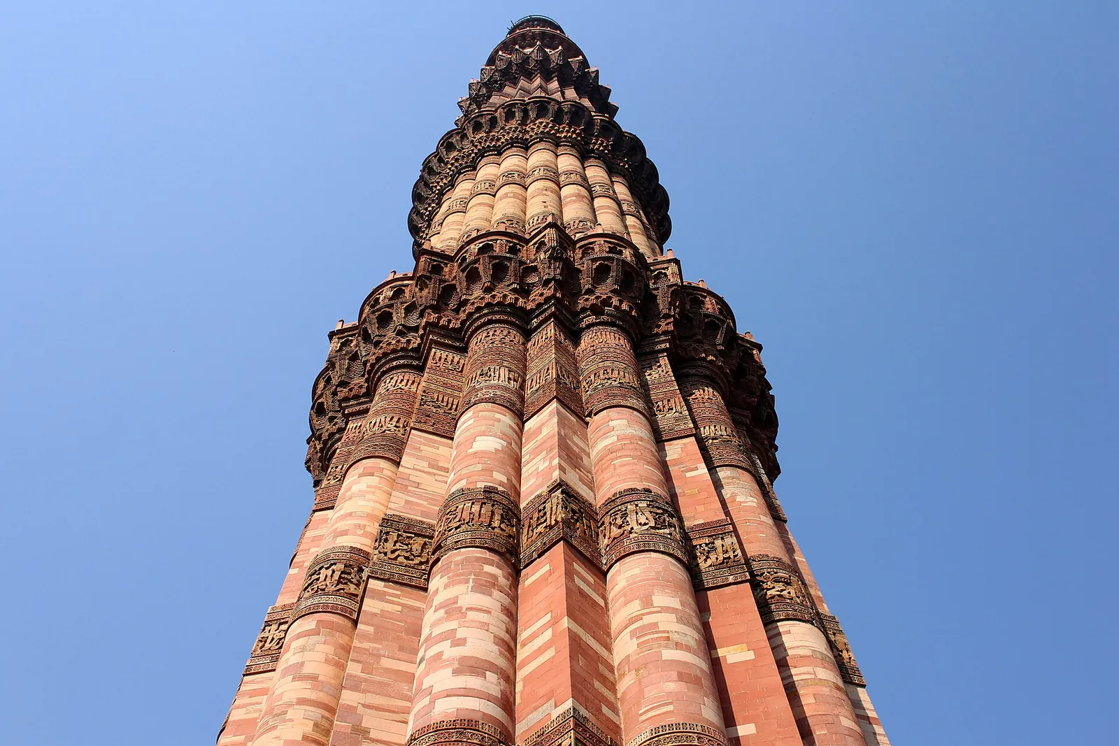 The carved red sandstone tower of Qutb Minar seen from its base against a blue sky