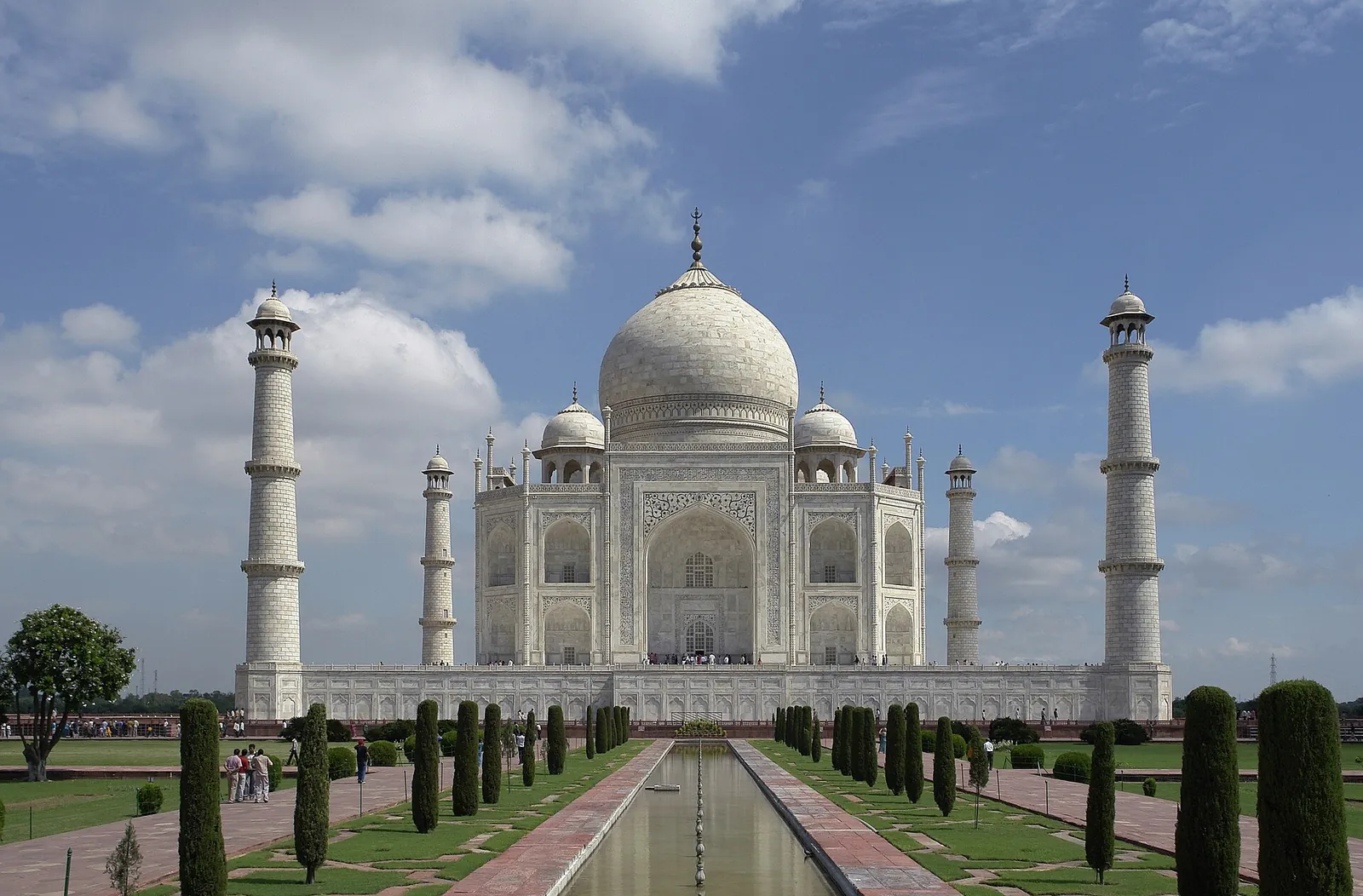 The Taj Mahal behind its long water channel and gardens under a blue sky