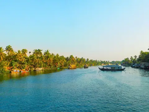Una casa flotante cruzando un ancho backwater azul bordeado de cocoteros en Kumarakom