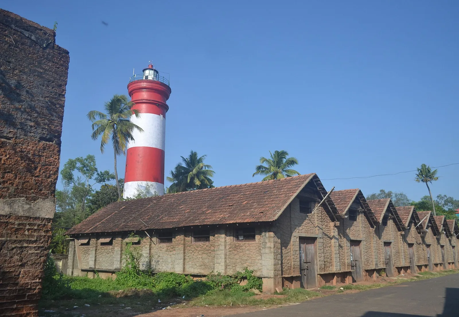 The red and white Alappuzha Lighthouse rising behind a row of old tiled warehouses
