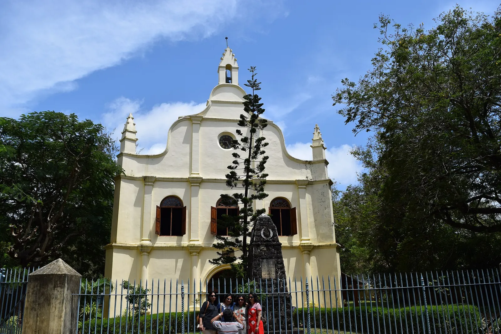 Fațada albă și galbenă a Bisericii Sfântul Francisc, în spatele gardului, sub un cer albastru, în Fort Kochi