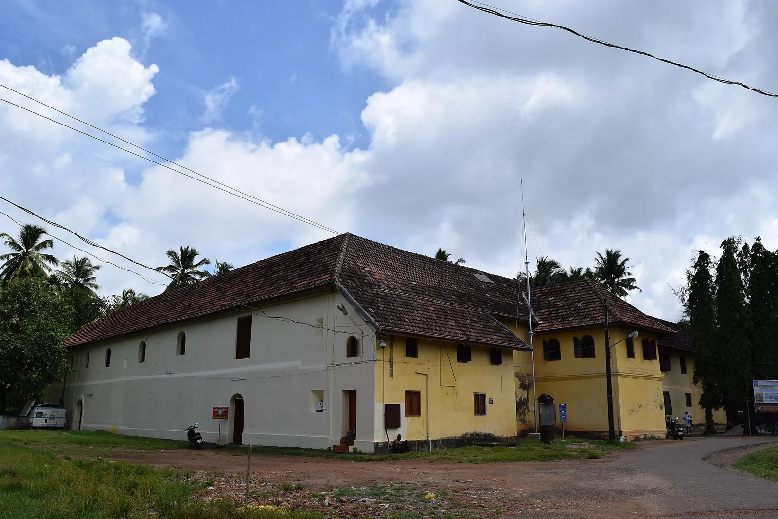 Clădire lungă, galbenă și albă, cu două niveluri și acoperiș de țiglă, sub nori, în Mattancherry