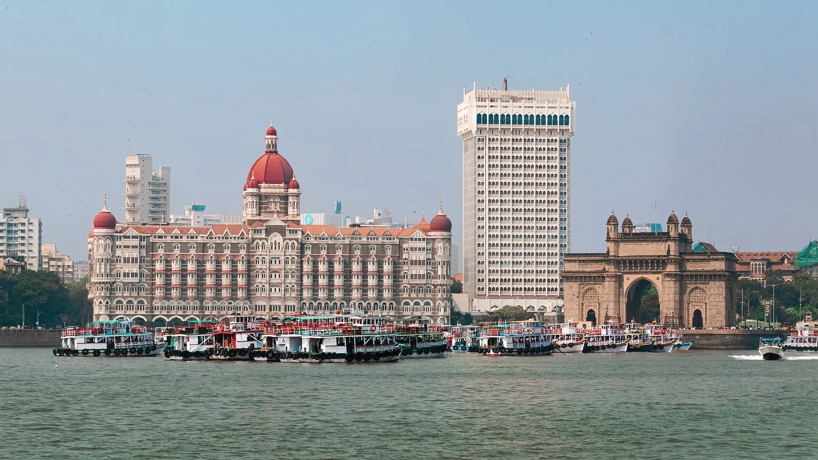 Arcul Gateway of India lângă faleza Colaba, văzut peste portul Mumbai, cu bărci în prim-plan