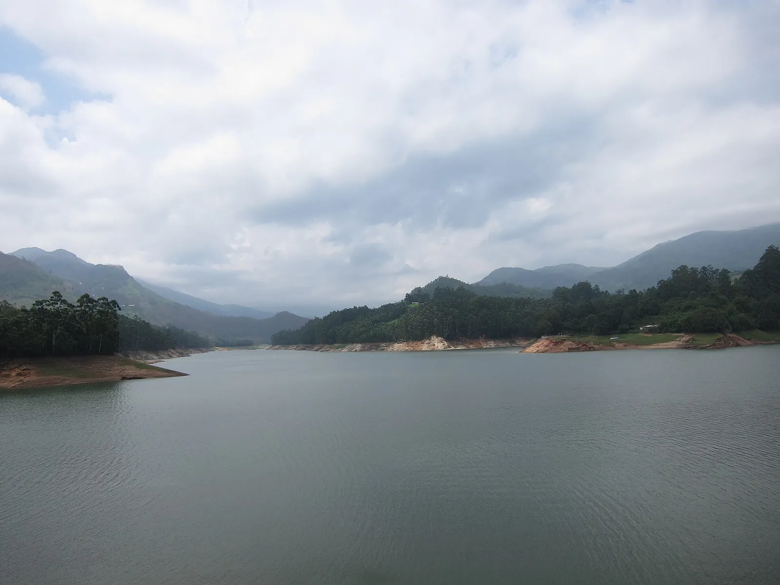 El amplio embalse de la presa de Mattupetty entre colinas boscosas bajo un cielo nublado