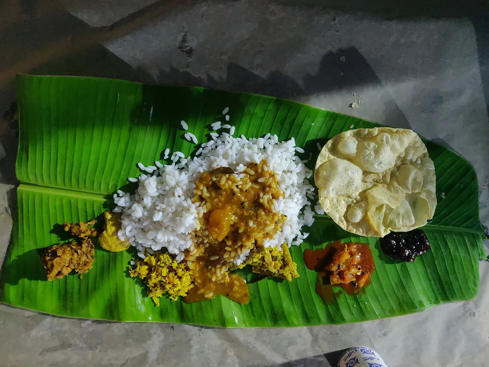 Un sadya de arroz, pappadam, encurtidos y platos de verduras servido sobre una hoja de plátano