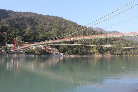 A Lakshman Jhula függőhíd a zöld Gangesz felett Rishikeshben, mögötte erdős dombok