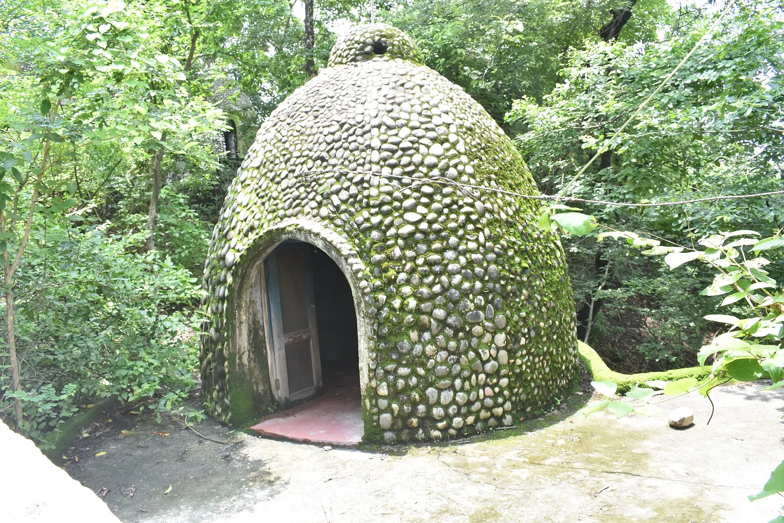 Eine gewölbte Meditationshütte aus Stein zwischen Bäumen im Beatles Ashram in Rishikesh