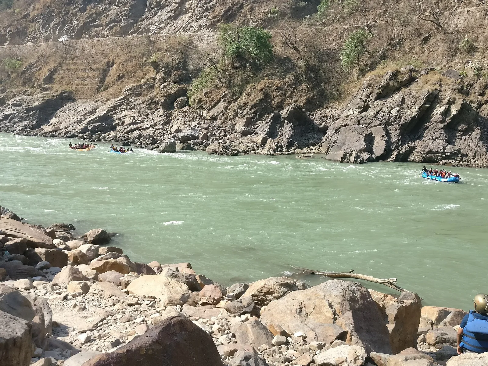 Schlauchboote in einer Stromschnelle auf dem grünen Ganga unterhalb felsiger Ufer bei Rishikesh