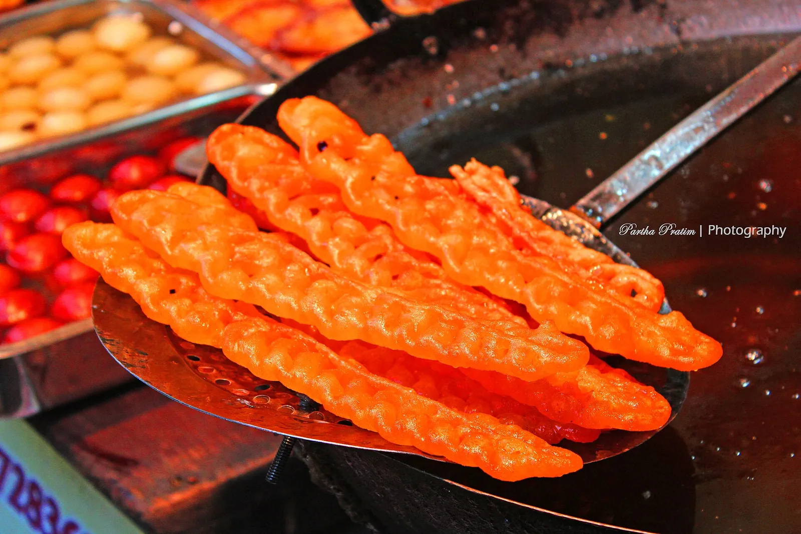 Orangefarbene Jalebi-Spiralen auf einer Frittierkelle an einem Süßwarenstand am Har Ki Pauri in Haridwar