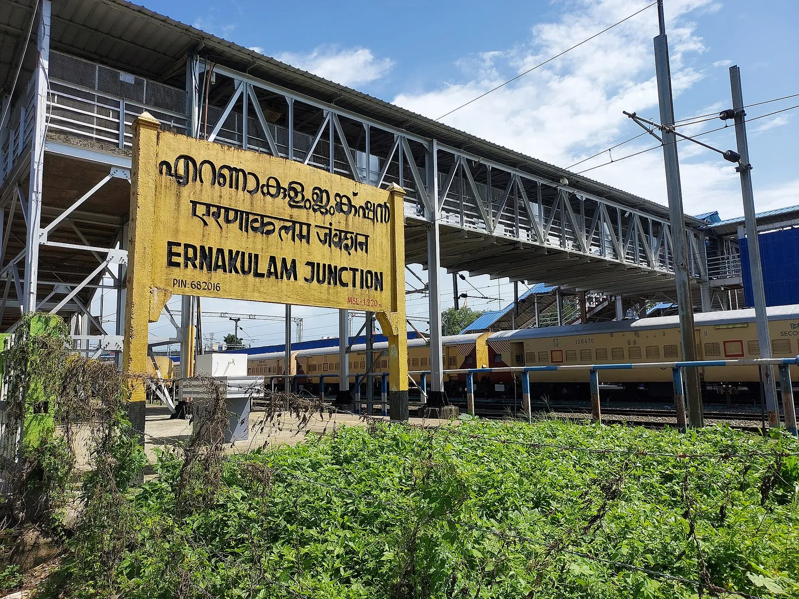 The yellow Ernakulam Junction station sign beside a platform and footbridge