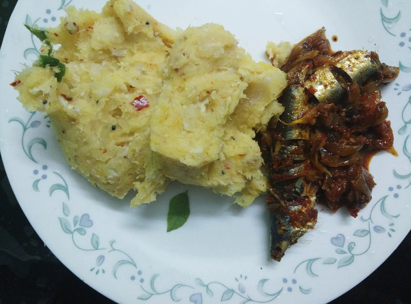 Mashed tapioca beside sardines in a red fish curry on a plate