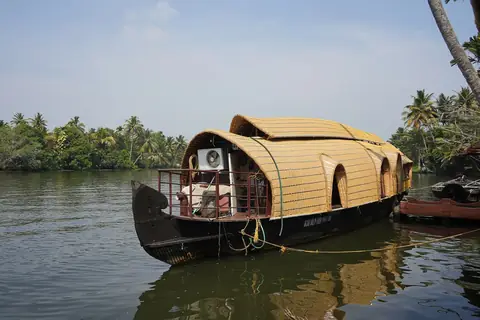 Kéralský hausbót se slaměnou střechou přivázaný na backwaters u Nedumudy, s palmami podél břehu