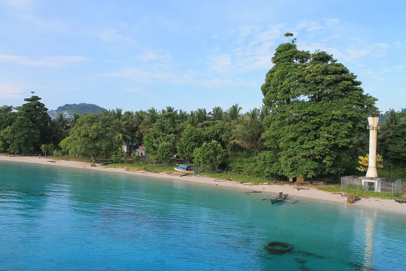 Turquoise water and a white-sand shore with trees at the jetty in Liang village on Ambon's east coast