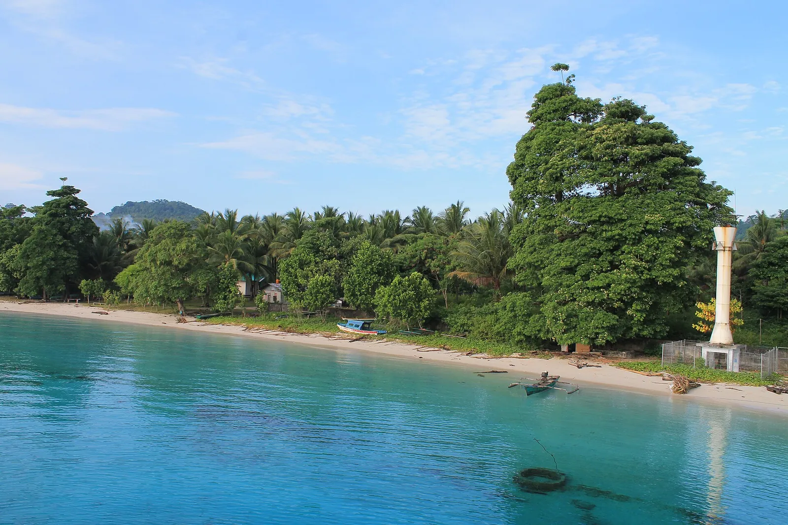 Turquoise water and a white-sand shore with trees at the jetty in Liang village on Ambon's east coast