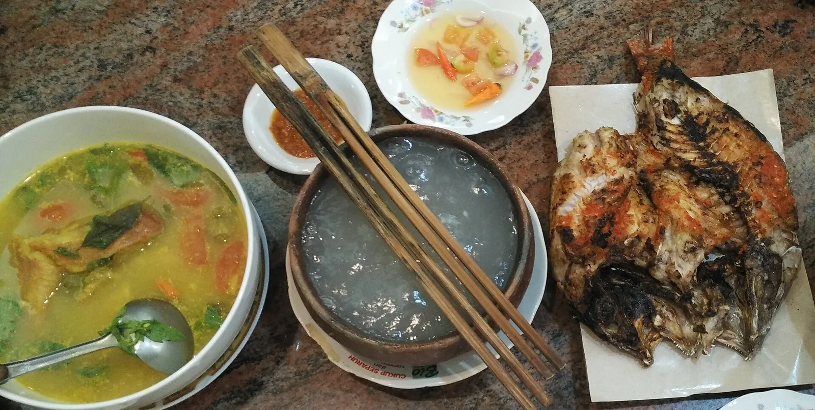 Papeda sago porridge with chopsticks, fish in yellow broth, grilled fish and colo-colo sambal on a table
