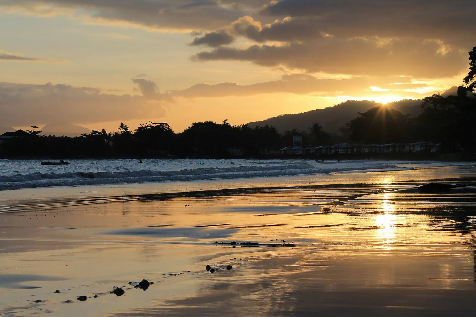 Sunset over the calm water and wet sand of Natsepa beach, with hills behind