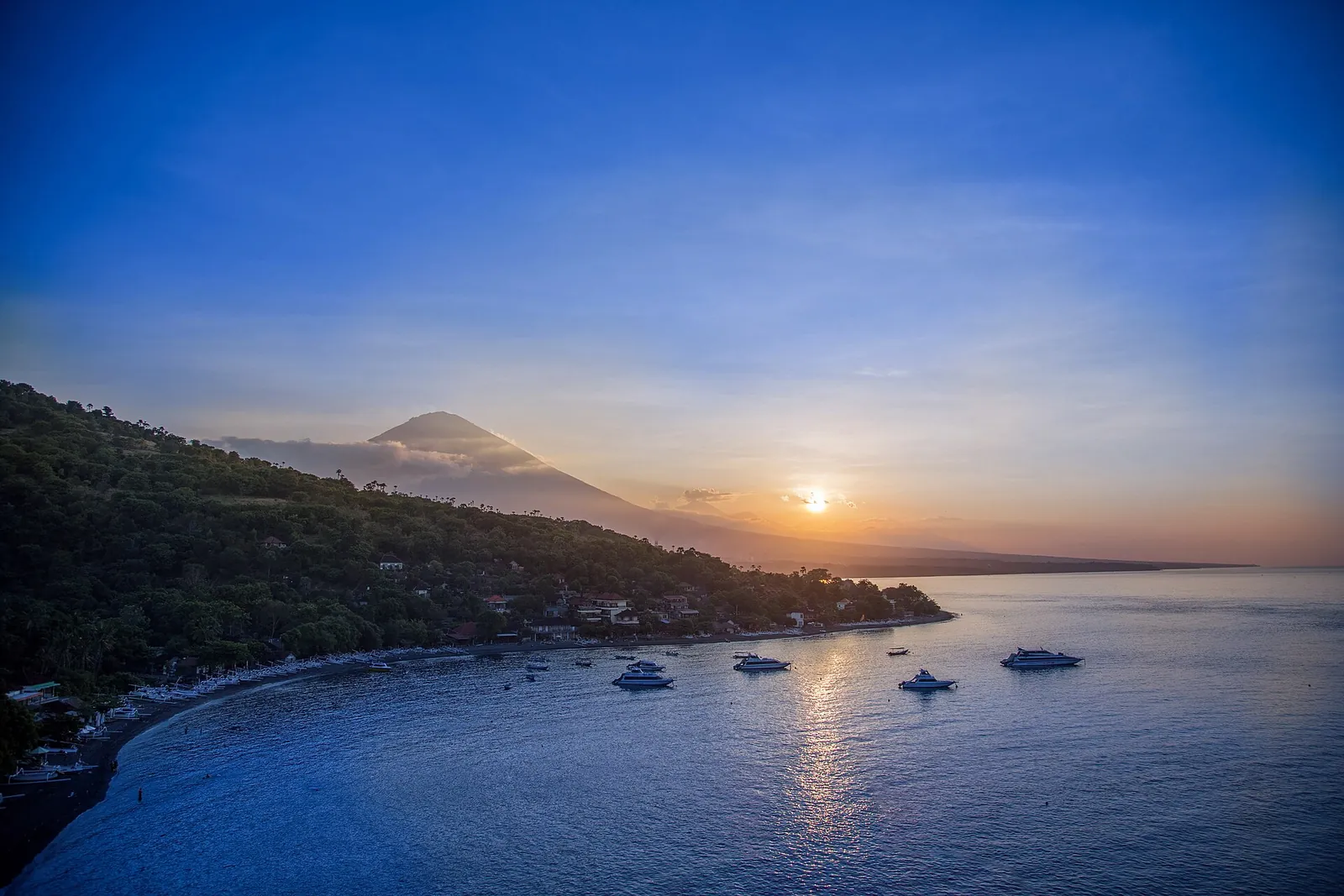 Amed bay at golden hour, with Mount Agung on the horizon, a low sun and boats moored on the calm sea