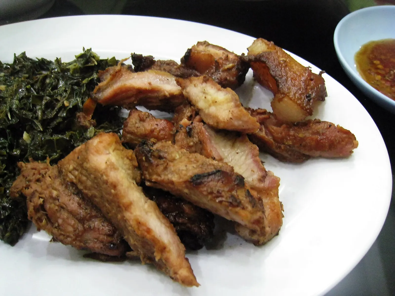 Pieces of smoked pork se'i babi on a plate with sauteed greens