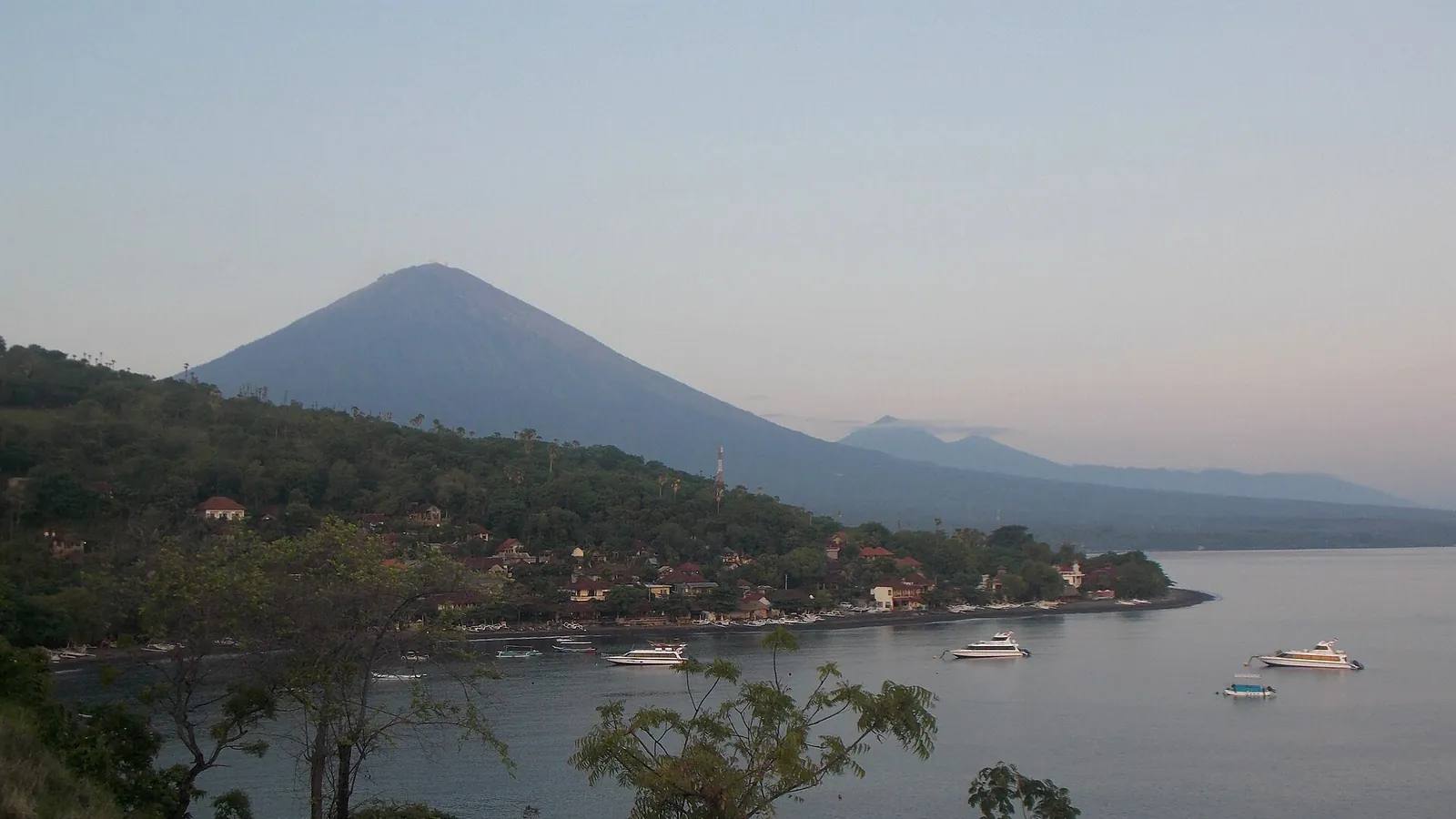 The cone of Mount Agung rising above the bay at Amed, with boats moored on calm water