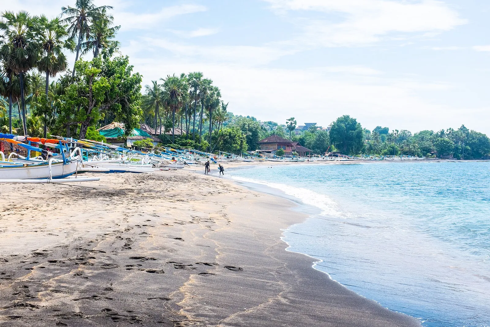 Colourful jukung outrigger boats drawn up on a sandy beach in an Amed fishing village, with palms along the shore