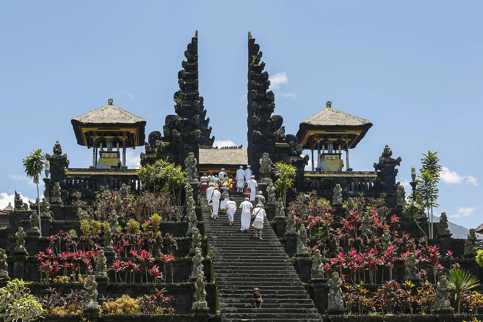 Worshippers in white climbing the steps between the split gates of Pura Besakih, lined with flowers