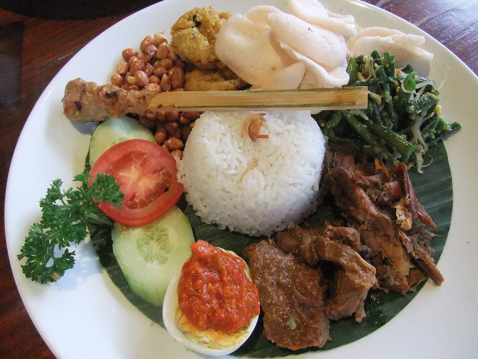 A plate of nasi campur with rice, duck, sate lilit, boiled egg, peanuts, sambal and vegetables on a banana leaf