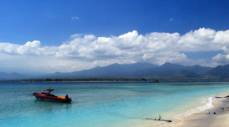 Turquoise shallows off the east coast of Gili Air with a small boat and the mountains of Lombok behind