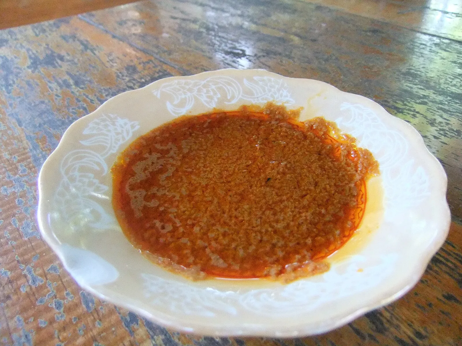 A white plate of red-orange Taliwang chilli sambal on a wooden table
