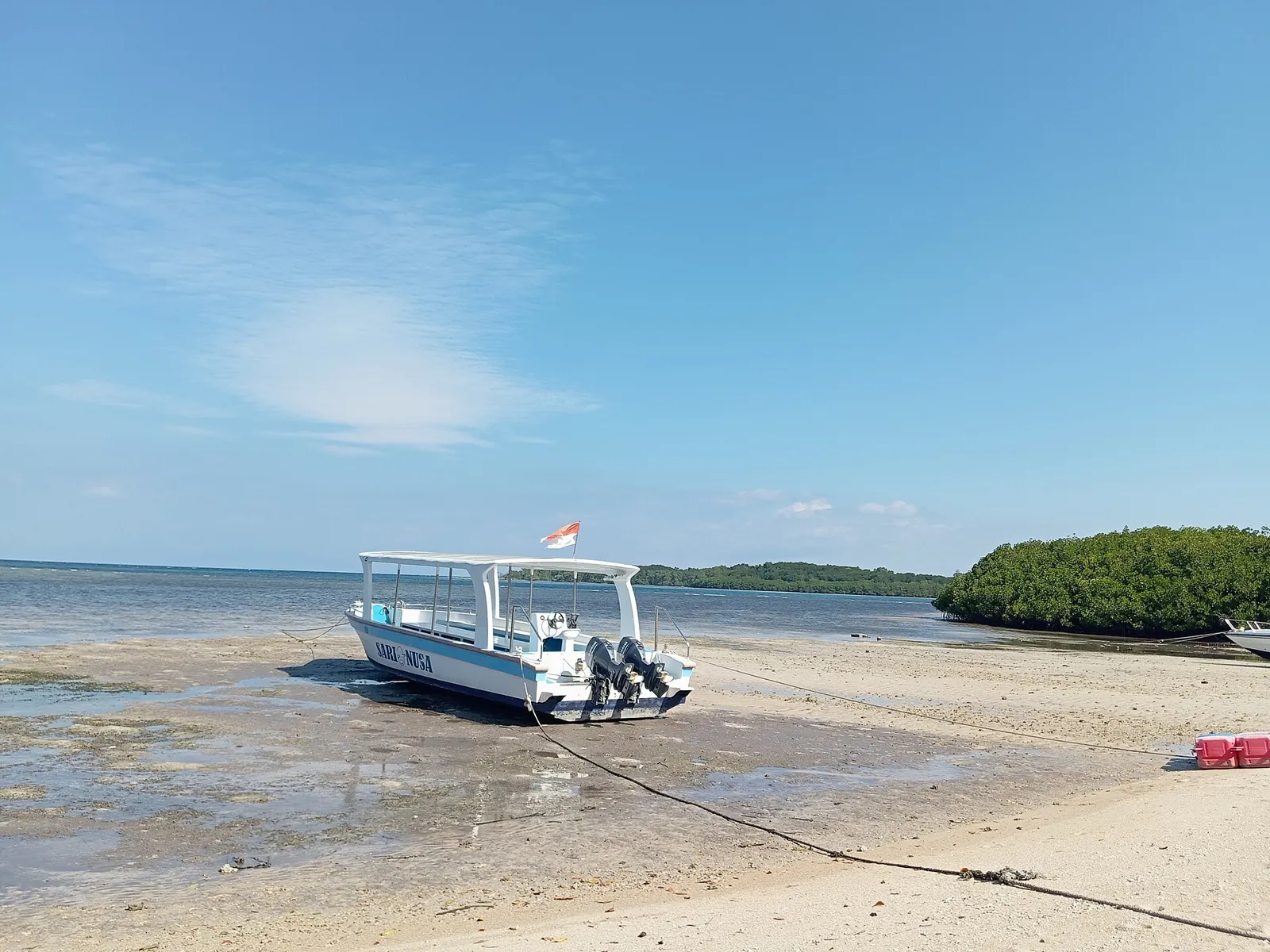 A small white boat pulled up on a sandy beach with mangroves and calm sea behind