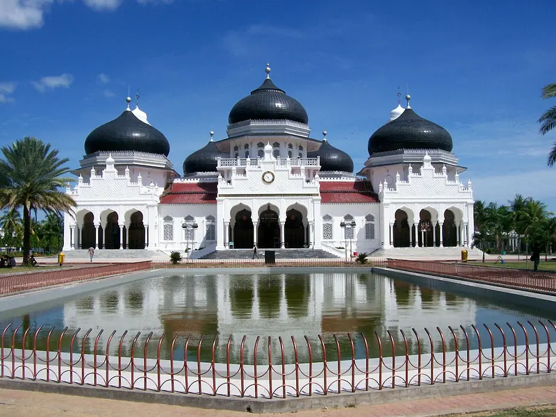 Baiturrahman Grand Mosque in Banda Aceh with white walls and black domes reflected in its courtyard pool