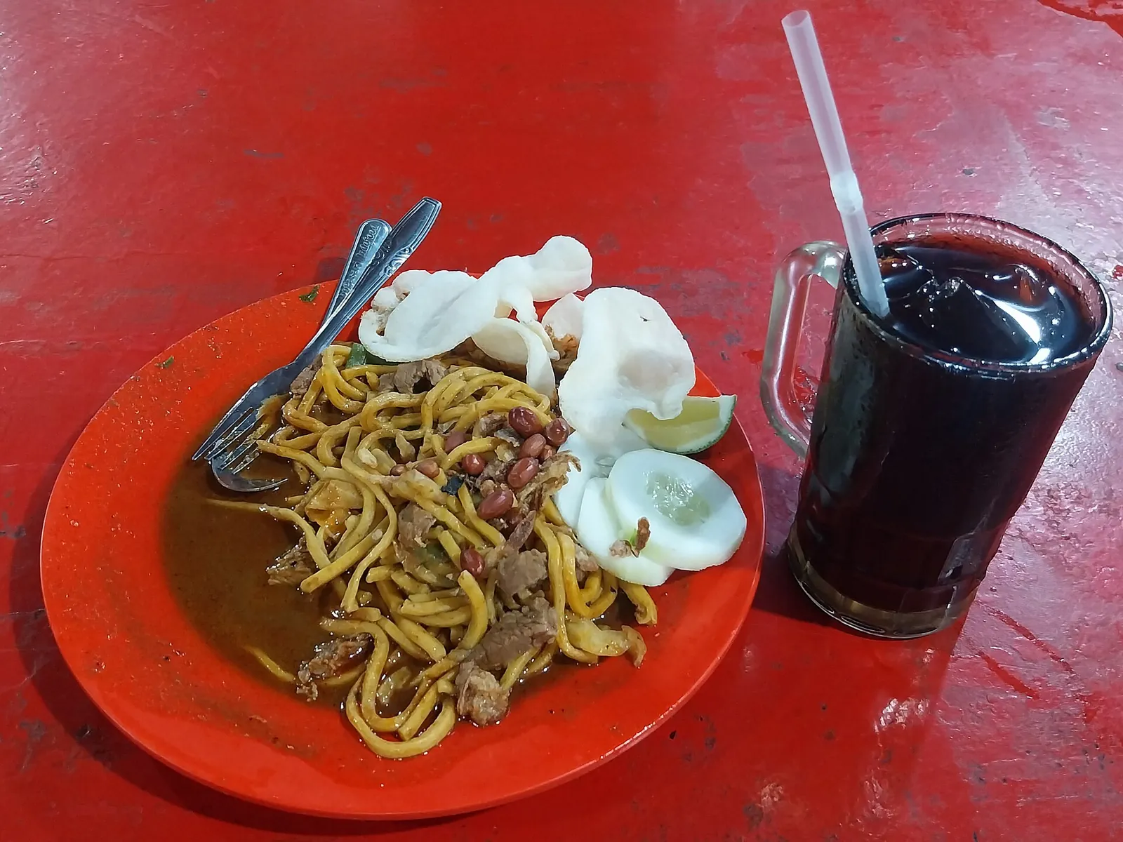 Plate of Mie Aceh noodles with crackers and cucumber beside a glass of Gayo coffee