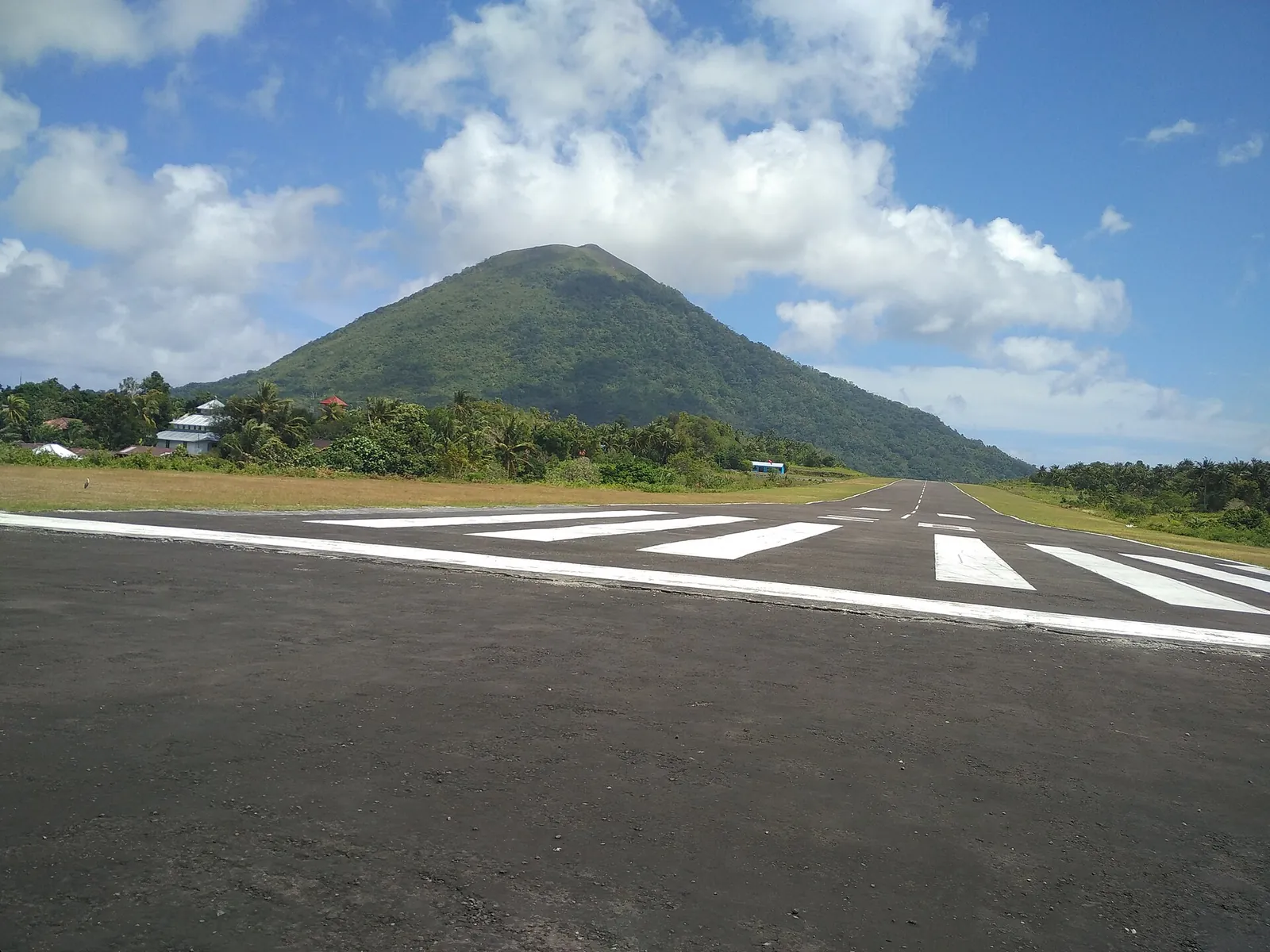 The runway of Banda Neira airport with the cone of Gunung Api behind it under a blue sky
