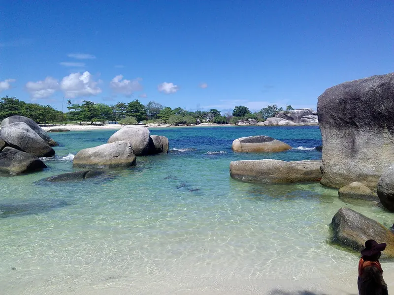 Clear turquoise shallows and grey granite boulders at Tanjung Tinggi Beach on Belitung under a blue sky