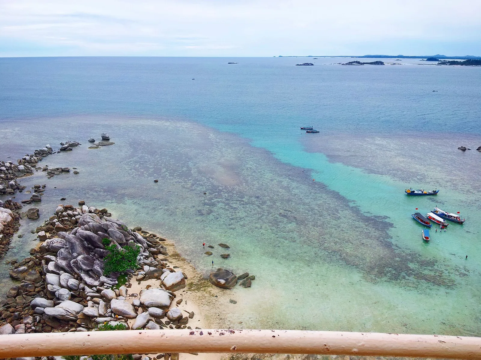 View from the top of the Lengkuas Island lighthouse over granite rocks, white sand, shallow turquoise water and moored boats