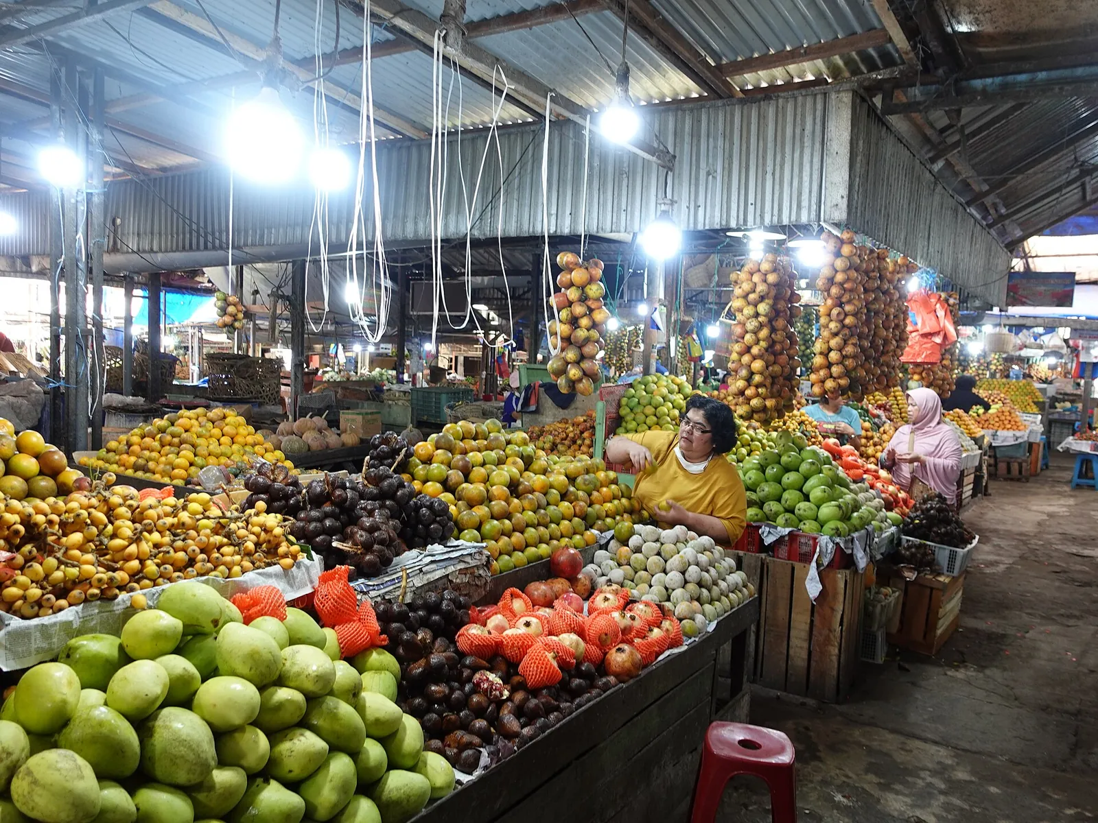 Stalls piled with oranges, limes, tomatoes and other fruit under a roof at Berastagi's fruit market