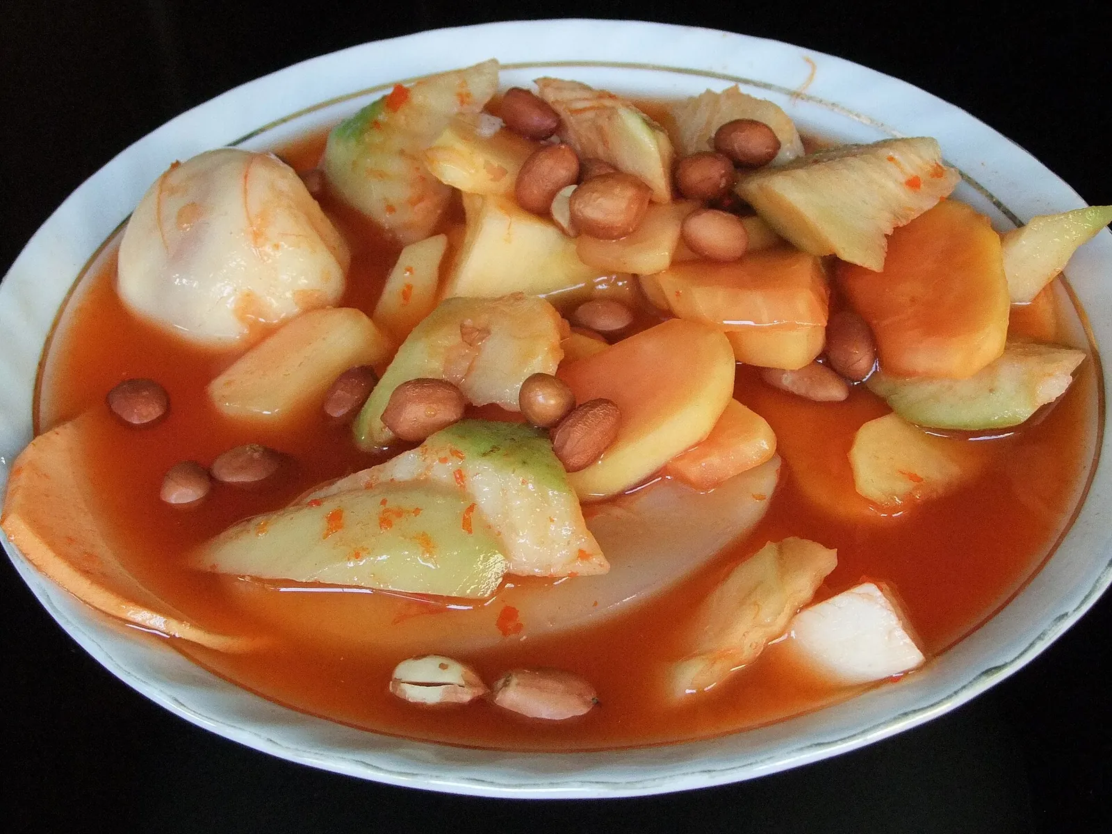 A plate of asinan Bogor: pieces of pickled fruit and peanuts in a red dressing