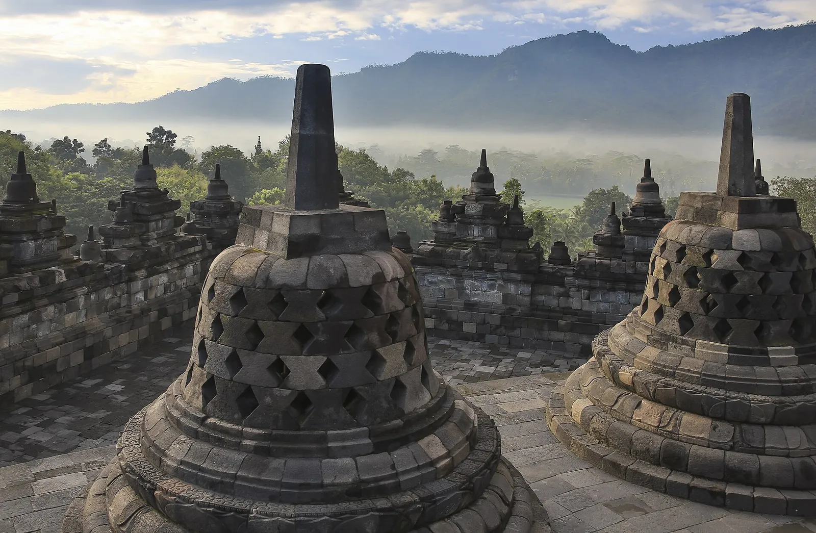 Perforated bell-shaped stupas on Borobudur's upper terrace with misty Menoreh hills behind