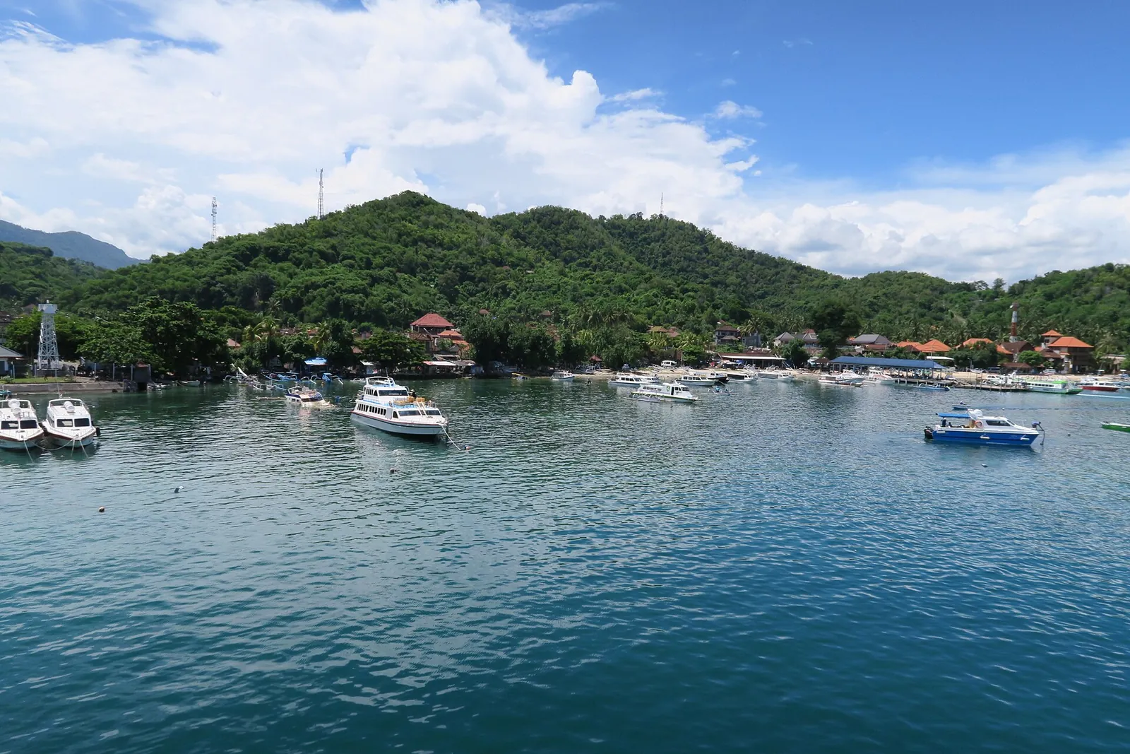 Boats moored in the calm bay at Padang Bai harbour in east Bali, with green hills behind