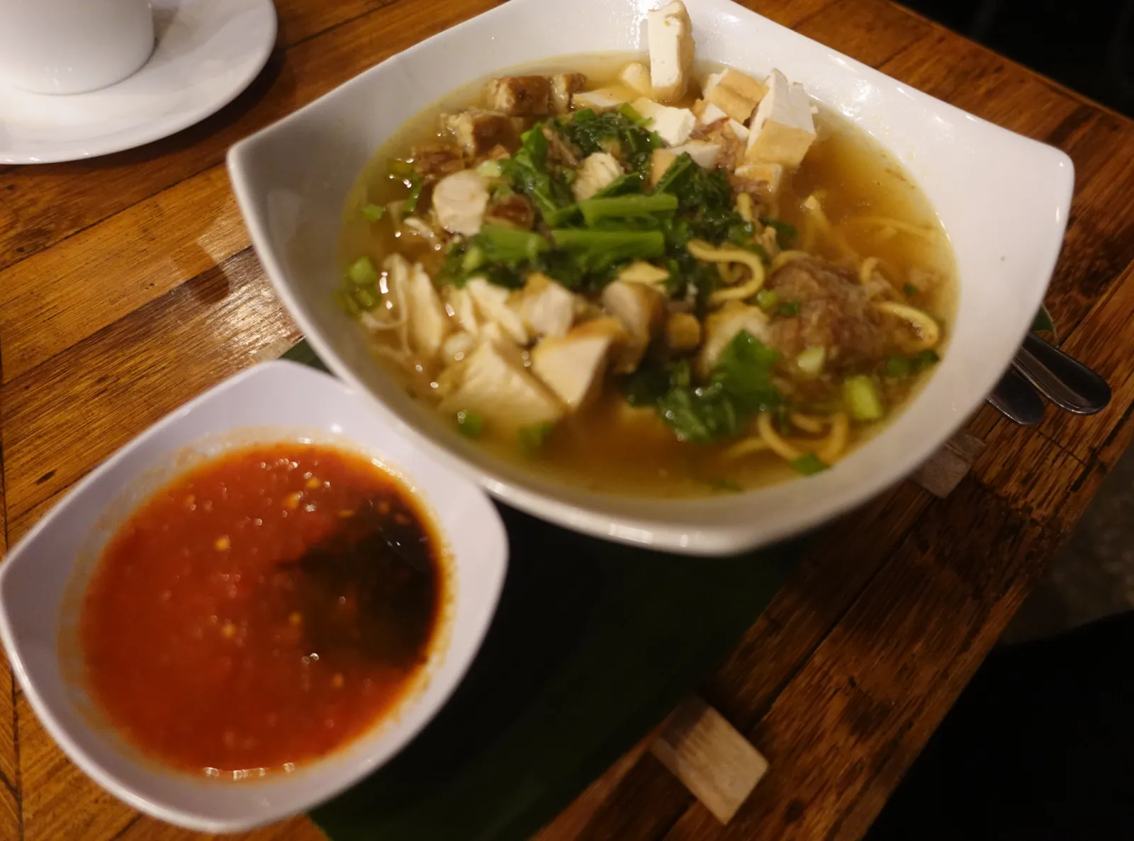 A bowl of mie sop ayam, chicken noodle soup with greens, and a dish of chilli sambal at a lodge in Bukit Lawang
