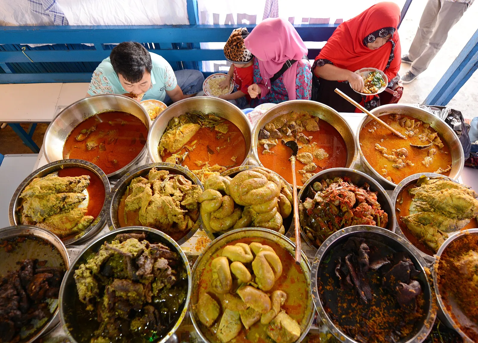 Rows of metal bowls holding curries, jackfruit gulai and other nasi kapau dishes on a stall counter