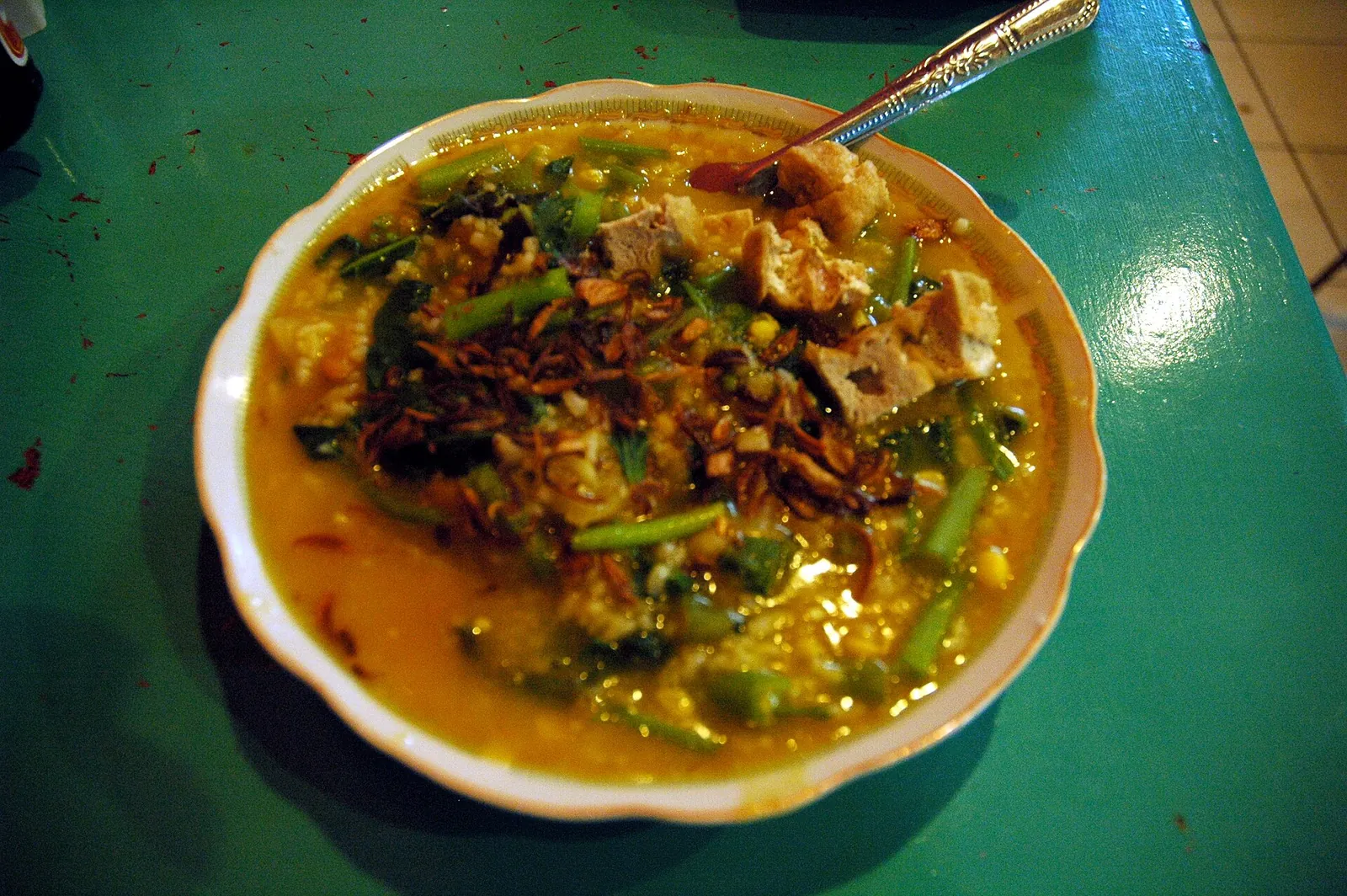 A bowl of tinutuan, Manado's vegetable rice porridge, topped with greens and fried shallots