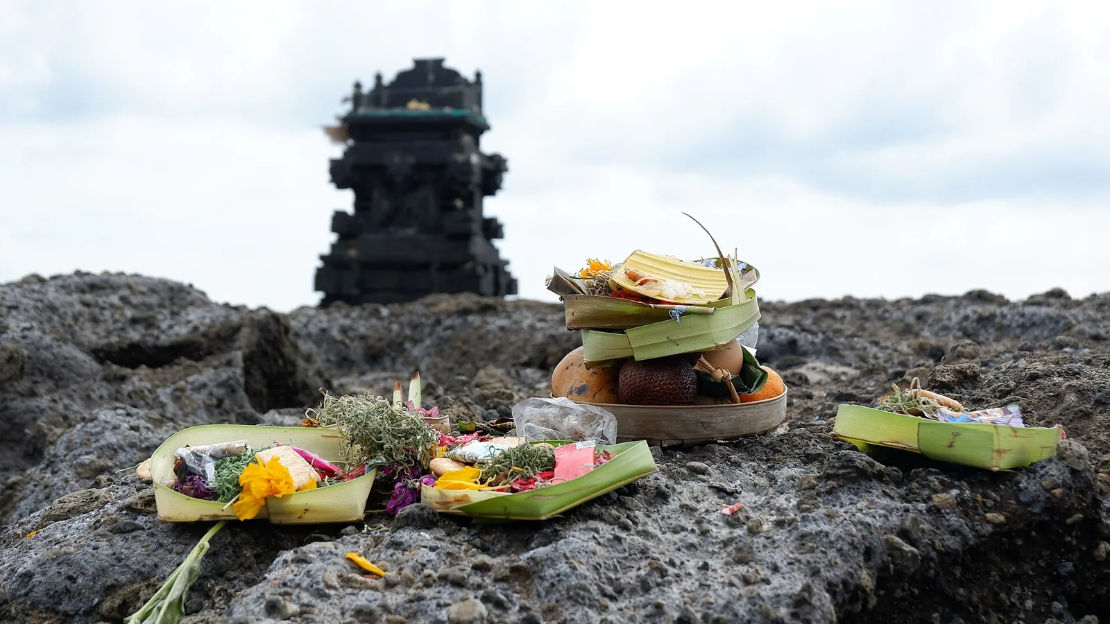 Balinese offerings of flowers and palm-leaf trays on a rock below a small stone shrine at Canggu Beach