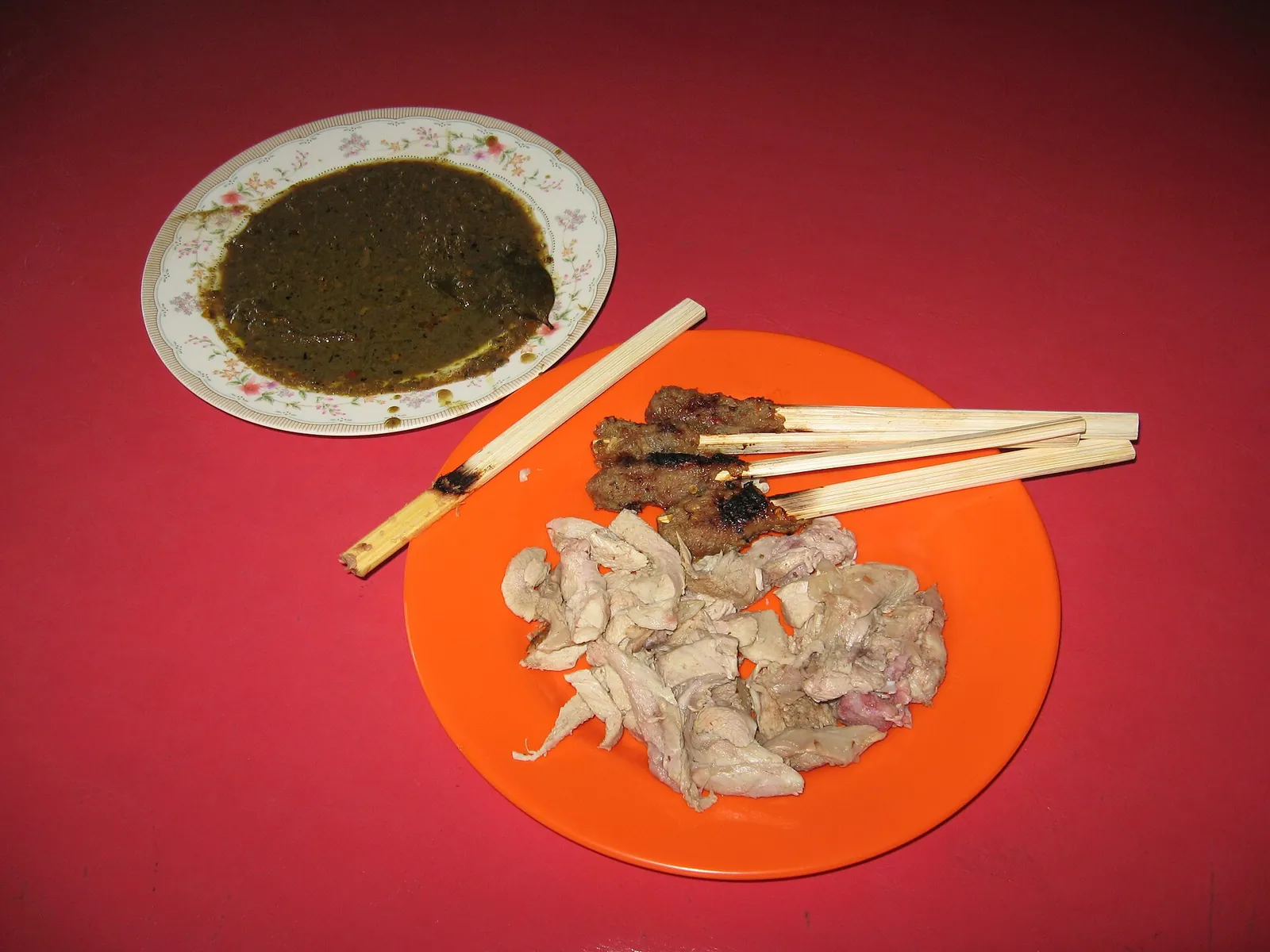 Roast pork babi guling and chicken sate lilit skewers on an orange plate, with a bowl of dark sauce