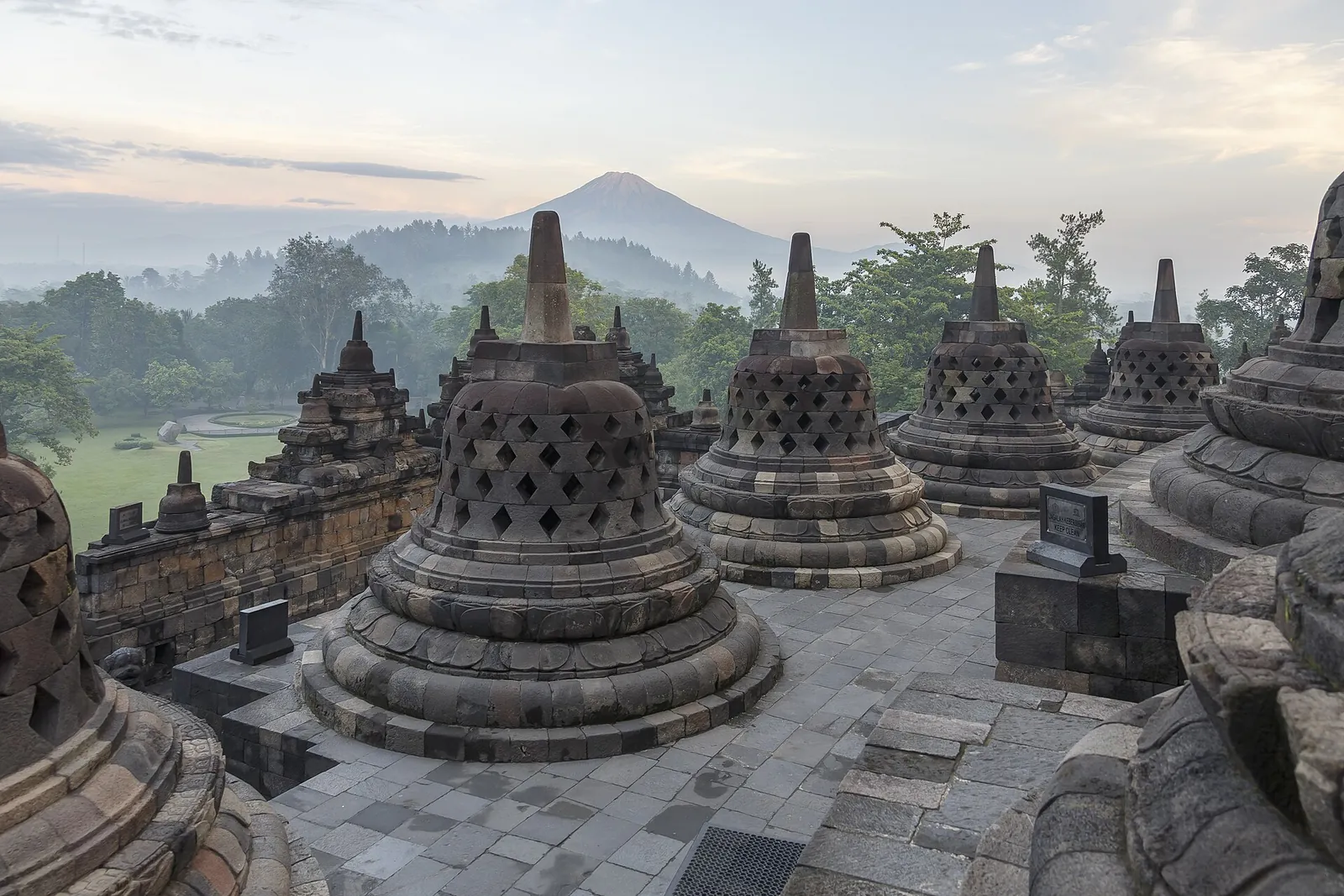 Perforated stupas on the upper circular terraces of Borobudur, with a volcano on the misty horizon